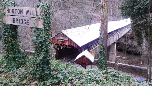 A wooden covered bridge named Horton Mill Bridge, surrounded by trees and ivy, in a scenic, wooded area.