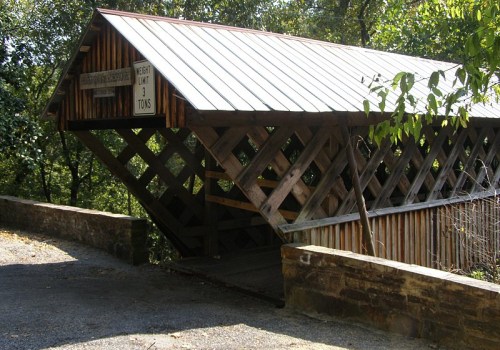 A wooden covered bridge with a metal roof, surrounded by trees, featuring a weight limit sign.