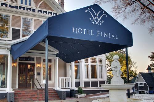 Entrance of Hotel Finial with a blue awning and a fountain in front, showcasing a charming architectural style.
