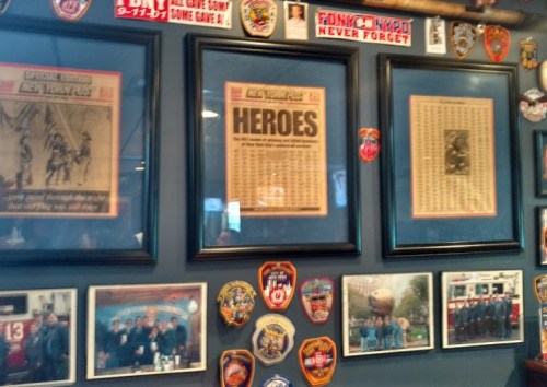 Framed newspaper clippings and photos on a wall, honoring heroes and firefighters, with various patches displayed.