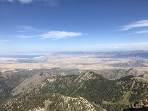 A panoramic view of mountains and valleys under a clear blue sky, with distant ranges and a flat landscape below.