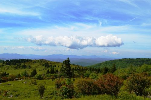 A scenic landscape featuring rolling green hills, distant mountains, and a blue sky with fluffy white clouds.