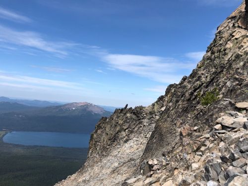 A rocky mountain ridge with a clear blue sky and a lake visible in the valley below.