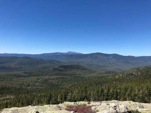 A panoramic view of lush green mountains under a clear blue sky, with distant peaks visible on the horizon.