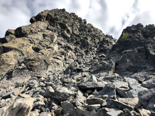 A steep rocky slope with scattered boulders under a cloudy sky.