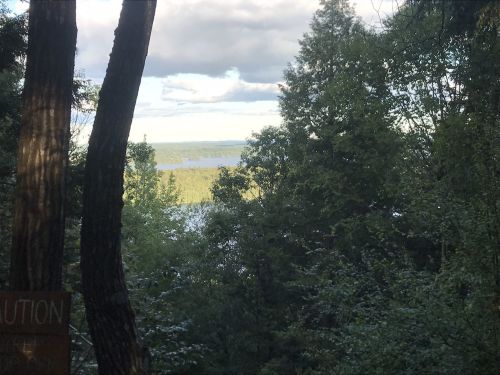 A scenic view of a lake surrounded by trees, with clouds in the sky and sunlight filtering through the foliage.