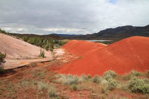 Vibrant red hills with green shrubs under a cloudy sky, showcasing a unique landscape.