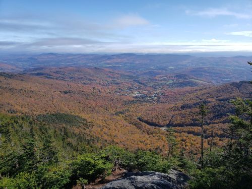 A panoramic view of a colorful autumn landscape with rolling hills and valleys under a clear blue sky.
