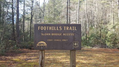 Sign for Foothills Trail at Sloan Bridge Access, indicating foot travel only, surrounded by trees and natural scenery.