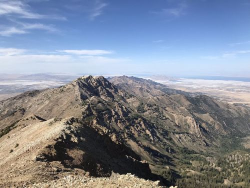 A panoramic view of rugged mountains under a clear blue sky, with valleys and distant plains visible in the background.
