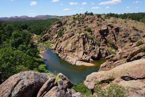 A scenic view of a winding river surrounded by rocky cliffs and lush greenery under a clear blue sky.