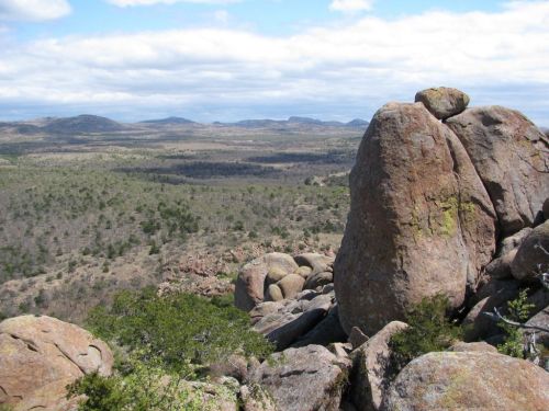 A rocky landscape with large boulders in the foreground and rolling hills in the background under a cloudy sky.