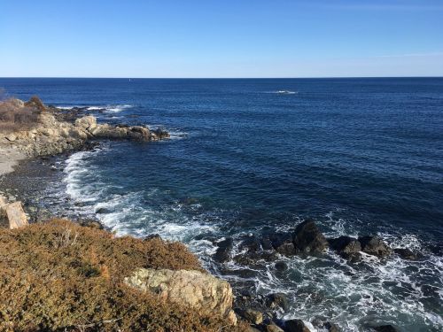 A serene coastal view with rocky shores and gentle waves under a clear blue sky.