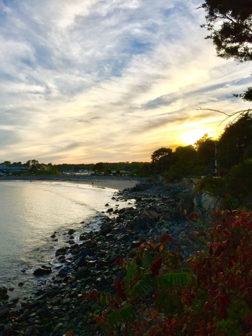 A serene beach scene at sunset, with rocky shorelines and a colorful sky reflecting on the water.