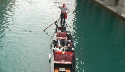 A gondola with six people enjoying a ride on a serene canal, guided by a gondolier in traditional attire.