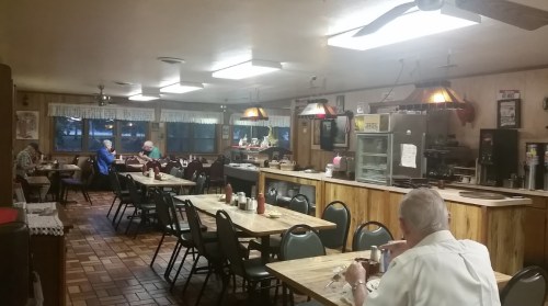 A cozy diner interior with wooden decor, tables, and patrons enjoying their meals. Warm lighting creates a welcoming atmosphere.