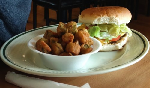 A plate with a sandwich topped with lettuce and tomato, alongside a bowl of fried okra.