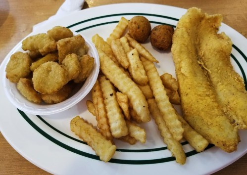 A plate with crinkle-cut fries, fried fish fillet, hushpuppies, and a side of fried nuggets.