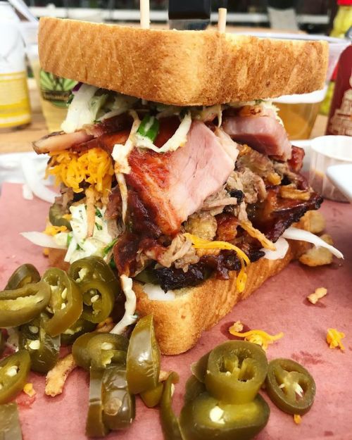 A towering sandwich filled with layers of meat, cheese, and coleslaw, served with sliced jalapeños on the side.