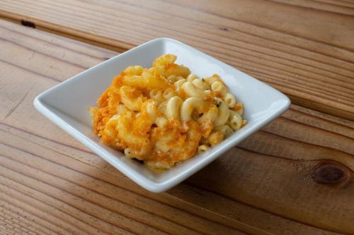 A small white bowl filled with creamy macaroni and cheese on a wooden table.