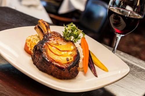 A beautifully plated ribeye steak topped with sliced peaches, accompanied by colorful vegetables and a glass of red wine.