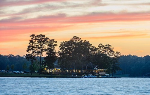 A serene lakeside view at sunset, featuring a restaurant surrounded by trees and a colorful sky.