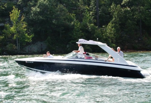 A speedboat with passengers cruising on a lake surrounded by trees.