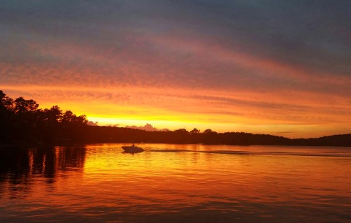 A serene sunset over a lake, with vibrant orange and purple hues reflecting on the water and a boat in the distance.
