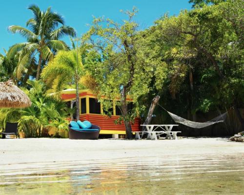 A colorful beach hut surrounded by palm trees, a hammock, and a picnic table on a sandy shore.