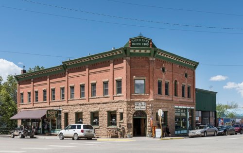 Historic brick building with green accents, featuring a café and shops, set against a clear blue sky.