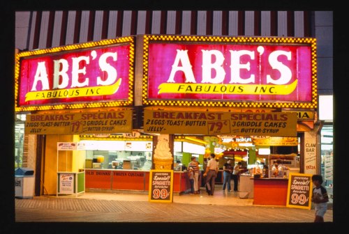 Brightly lit diner sign reading "Abe's Fabulous Inc." with menu specials and a bustling entrance.