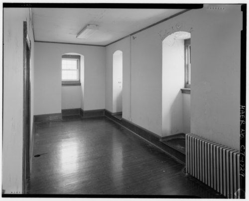 Interior view of a simple, empty room with wooden floors, windows, and a radiator along the wall.