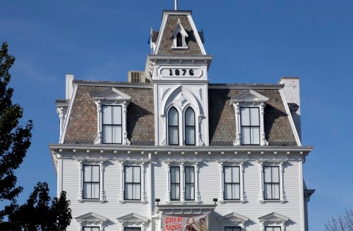 Historic white building with a steep roof, featuring decorative gables and the year "1876" prominently displayed.