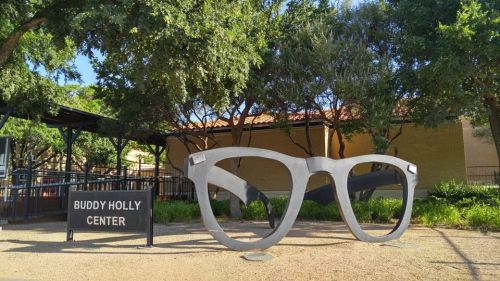 Large metal sculpture of glasses outside the Buddy Holly Center, surrounded by trees and greenery.