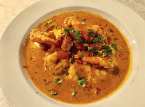 A bowl of shrimp and grits topped with green onions and spices in a creamy sauce.