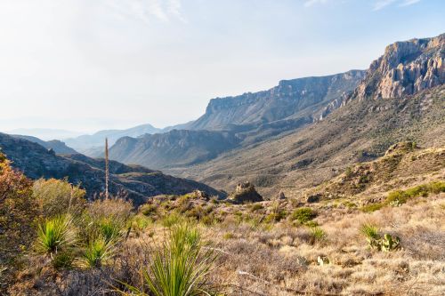A scenic view of a mountainous landscape with rolling hills and sparse vegetation under a clear sky.