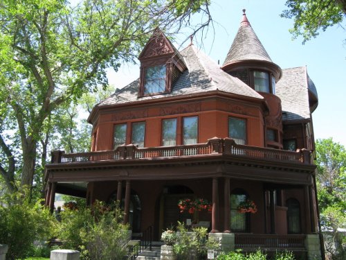 A large, ornate Victorian house with a turret, surrounded by trees and greenery on a sunny day.