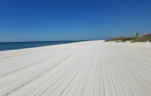 A serene beach with white sand, gentle waves, and a clear blue sky, stretching into the distance.