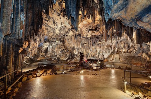 A vast cave interior with dramatic stalactites and stalagmites, illuminated by soft lighting along a winding path.