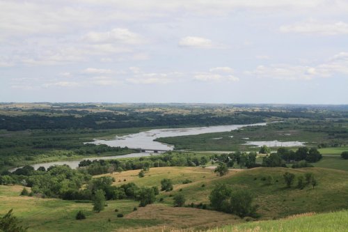 A scenic view of rolling green hills and a winding river under a partly cloudy sky.