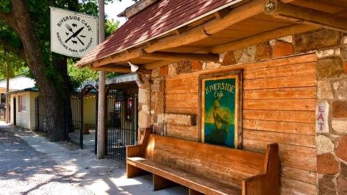Exterior of Riverside Café in Medicine Park, Oklahoma, featuring a wooden bench and a sign hanging above.