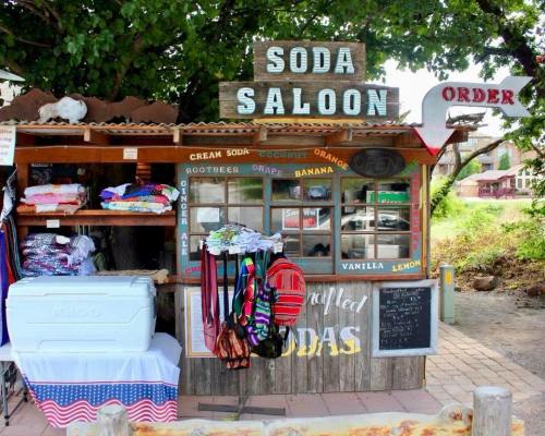 A colorful soda stand with various drinks and merchandise displayed outside under a tree.