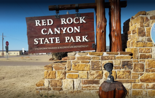 Sign for Red Rock Canyon State Park in Oklahoma, featuring stone structure and nearby stop sign.