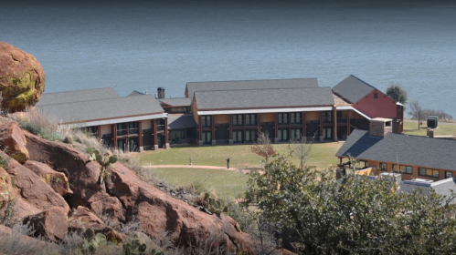 A scenic view of a lakeside lodge surrounded by rocky terrain and greenery.