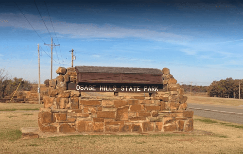 Sign for Osage Hills State Park made of stone, set against a clear blue sky and grassy landscape.