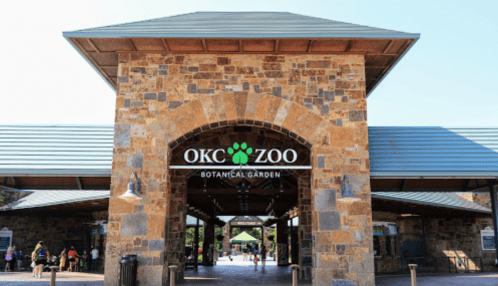 Entrance to the OKC Zoo and Botanical Garden, featuring a stone archway and a clear blue sky.