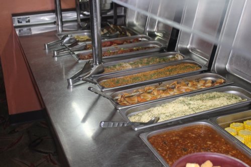 A buffet line featuring various dishes in metal trays, including rice, beans, vegetables, and chicken.