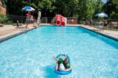 Children enjoying a sunny day at a pool, with water slides and others playing nearby.