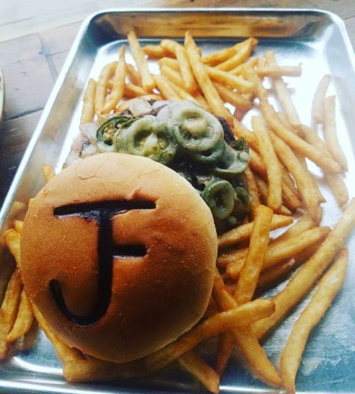 A tray with a burger topped with jalapeños and a bun marked "J," accompanied by a side of golden fries.