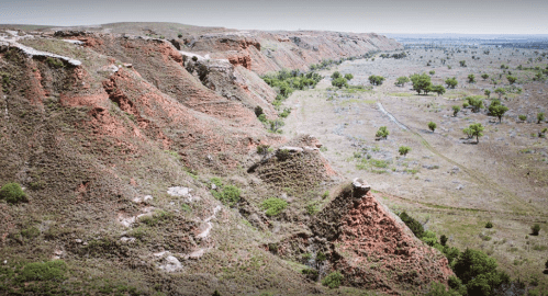 A panoramic view of rugged red cliffs and a grassy valley under a clear sky, showcasing natural landscape features.